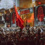 A large crowd participates in a religious ceremony at a notable landmark in Karbala, Iraq.