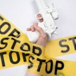 White toy gun held by hand wrapped with yellow stop tape, representing a call for nonviolence.