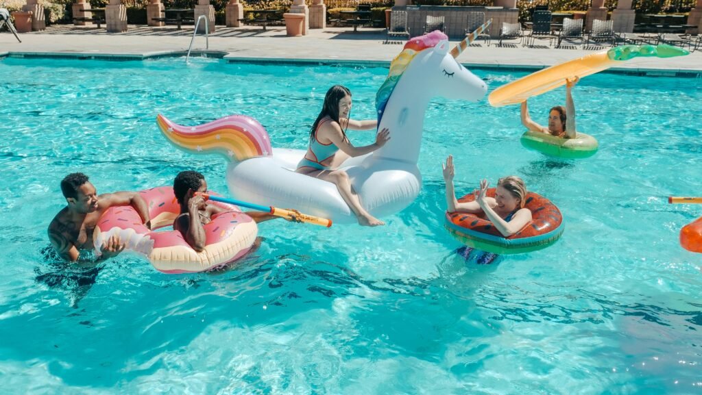 Group of adults enjoying a summer pool party with colorful inflatable floats and water guns.