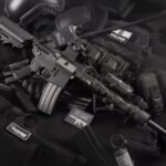 Close-up of tactical military gear including a rifle, radio, and vest on a dark background.