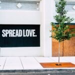 Street view with 'Spread Love' mural and a young tree on a sidewalk.