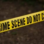 Close-up of crime scene tape with 'Do Not Cross' text, outdoors setting.